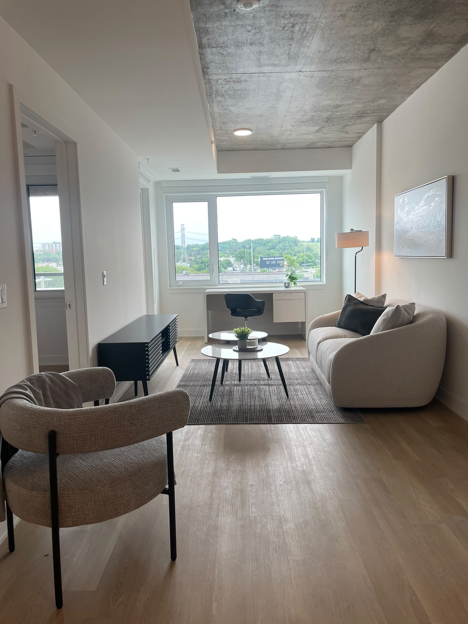 Bright furnished living room with sofa, accent chair, media console, and window-side desk