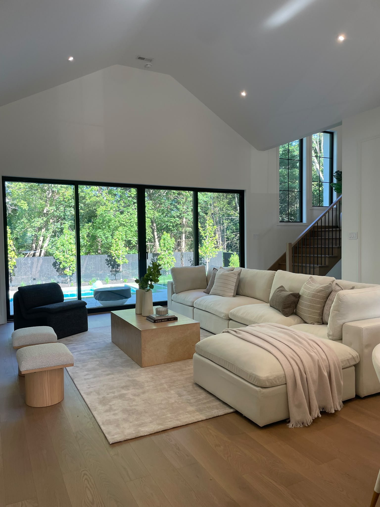Spacious living room with a cream sectional, high ceiling, staircase, and large garden-facing windows